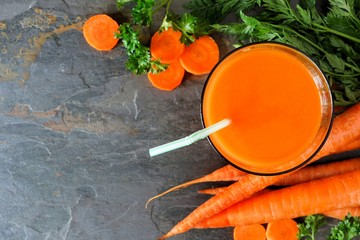 Wall Mural - Glass of fresh carrot juice, downward scene over a slate background