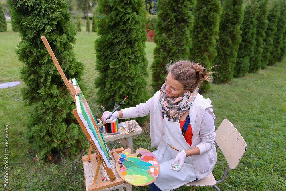 Girl artist paints picture and sits on chair at easel sides of t Stock ...