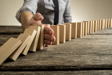 Man stopping domino effect on wooden table