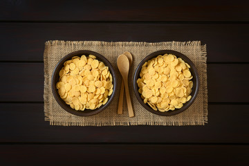 Wall Mural - Crispy corn flakes breakfast cereal in rustic bowls with small wooden spoons, photographed overhead on dark wood with natural light