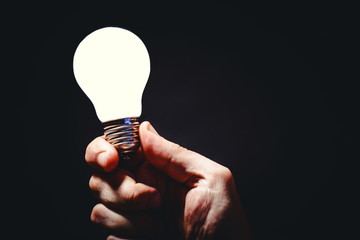 Wall Mural - Hand holding bright light bulb in fingers. Concept and idea background.