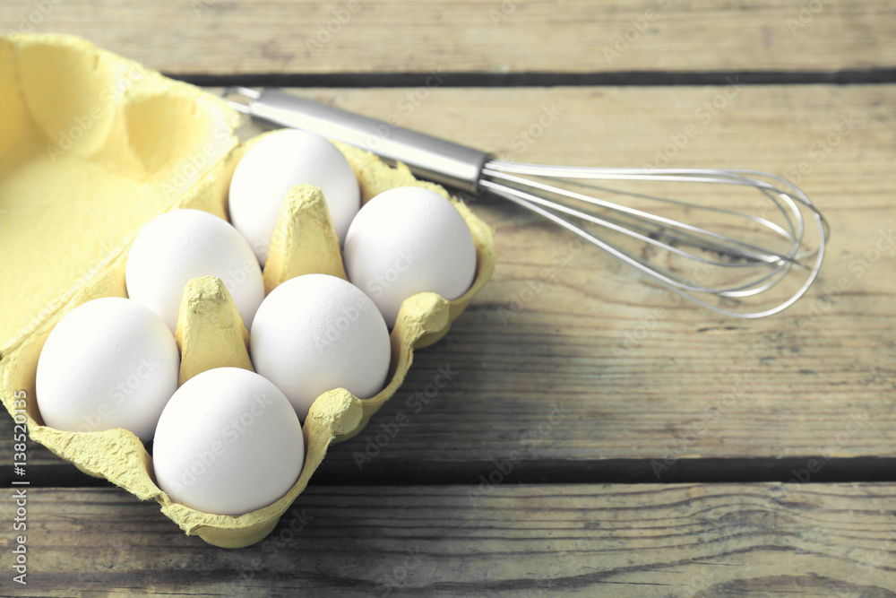 Raw eggs and whisk on wooden background
