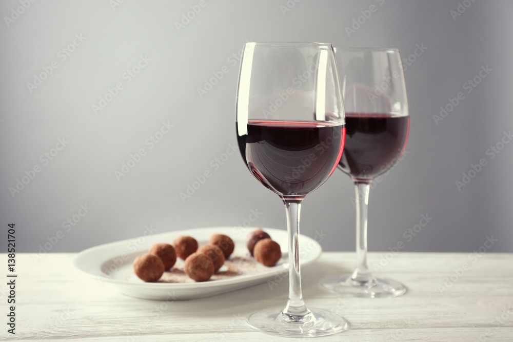 Chocolate truffles and glasses with red wine on white wooden table