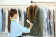 © Africa Studio - Woman with adhesive roller cleaning clothes in dry-cleaning salon