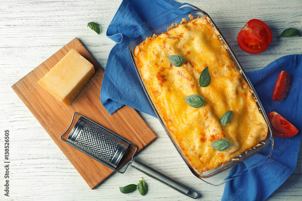 Traditional lasagna in glass baking dish, tomatoes and napkin on table