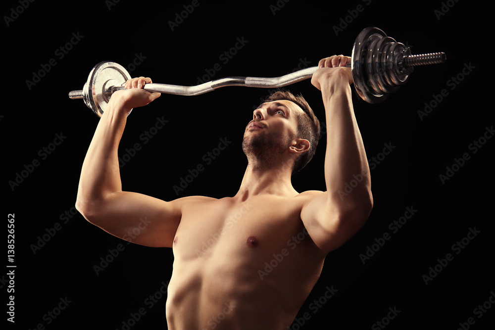 Sporty man doing exercises with barbell on black background