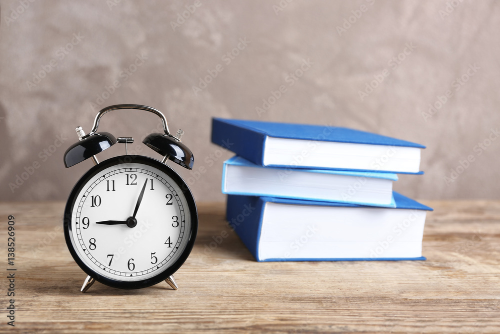 Alarm clock and stack of books on wooden table