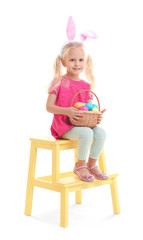 Wall Mural - Cute little girl with bunny ears and basket full of Easter eggs on white background