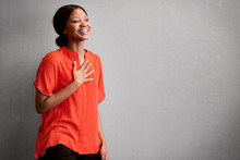 Black Female Business Person Busy Laughing With One Hand Against Her Chest While Wearing A Bright Colourful Orange Blouse With Space For Copy Text On The Right Of The Image.