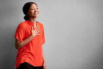 black female business person busy laughing with one hand against her chest while wearing a bright co