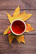 Autumn leaf with cup of tea on brown wooden table