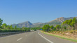 Sunshine on Coastal highway.  Lone white car drives along through foothills and mountain ranges on the edges of continental Europe in rural Spain. 