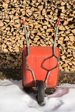 Old Wheelbarrow In Front Of A Pile Of Firewood On A Sunny Winter Day