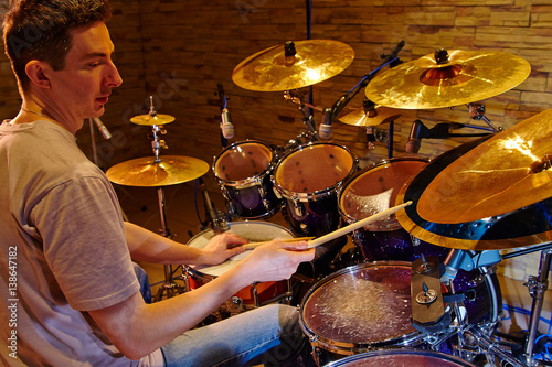 Zdjęcie XXL Widok z boku młodego perkusisty grającego zestaw perkusyjny w studio