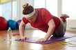 © pressmaster - Portrait of young obese woman working out on yoga mat in sunlit fitness studio: performing knee push up exercise with effort to lose weight