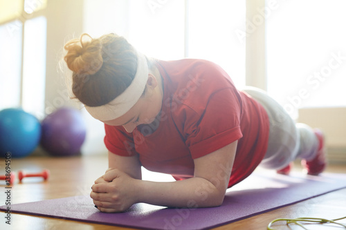 Fotomural Portrait of young obese woman working out on yoga mat in sunlit fitness studio: