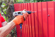 Metal fence installation. Work man in gloves with a drill builds new metal fence.