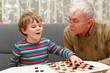 © Irina Schmidt - little kid boy and senior grandfather playing together checkers game