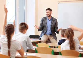 Wall Mural - Pupils listening teacher and raising hands to answer in classroom