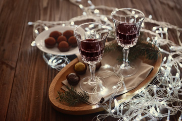 Wall Mural - Glasses of wine and chocolates on wooden table with garland, closeup