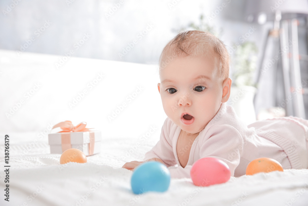 Cute little baby with Easter eggs lying on bed at home