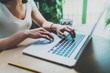 © SFIO CRACHO - Closeup view of young woman working at home on modern computer.Female hands typing on laptop keyboard while sitting at the wooden table.Blurred background.