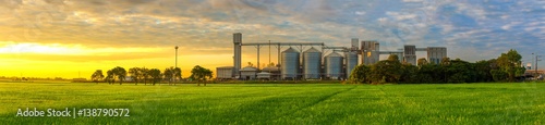 Fotografía Agricultural Silos - Building Exterior, Storage and drying of grains, wheat, corn, soy, sunflower against the blue sky with rice fields
