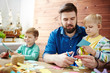 © pressmaster - Young handsome male teacher and two little boys with scissors in hands cutting from colorful paper in art class