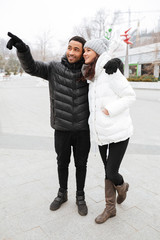 Wall Mural - Happy couple standing and pointing away at winter park