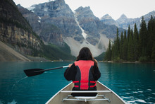 Person Paddling Canoe On Lake By Mountains 