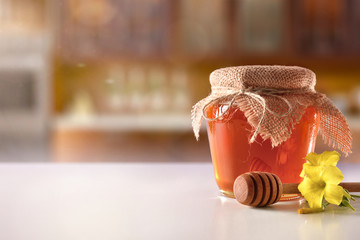 Glass pot with honey and dipper on white kitchen table