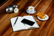 Notizbuch, Croissant und Kaffeetasse auf Holztisch