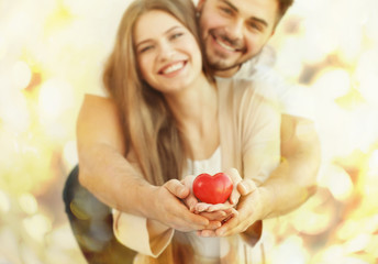 Canvas Print - Young couple holding small red heart, on light background