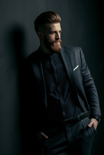 Stylish Handsome Bearded Man In Trendy Suit Standing With Hands In Pockets On Black