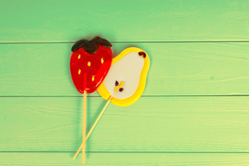 Tasty lollipops as a pear and strawberry on green board