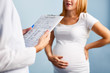 © pressmaster - Mid-section image of young pregnant woman talking to doctor in office, focus on folder with patients details in gynecologists hands
