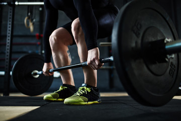 Low section of unrecognizable male athlete lifting huge heavy barbell from floor, leg muscles straining with effort