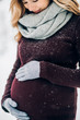Blonde pregnant lady in grey scarf and gloves smiles tender