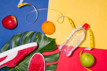 Wall Mural - Sport concept. Fitness equipment. Sneakers, water, apple, dumbbell on colorful background.