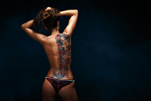 Back View Of Young Topless Woman Showing A Huge Tattoo On Her Back On The Black Background.