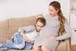 © Syda Productions - happy pregnant woman and girl on sofa at home