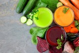 Three glasses of healthy vegetable juice with scattered ingredients, above view over a slate background