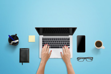 Leinwandbilder - Blue work desk in modern office. Woman writing on the laptop computer. Smart phone with blank screen for mockup beside.
