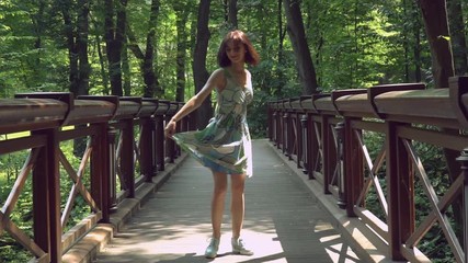 Poster - An attractive lady is whirling in the forest and bends her back across the wooden bridge afterwards. Her spring colored dress is waved during the spins.