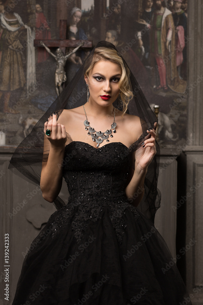 beautiful blonde woman in a black evening dress stands on a background of  the altar and