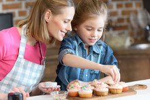 Side View Of Daughter And Mother Decorating Cupcakes With Confetti
