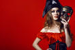 Portrait of gorgeous sexy woman with provocative make-up in pirate costume holding skull mask next to her face. Gamble and casino concept. Isolated on bright red background. Close up. Copy-space