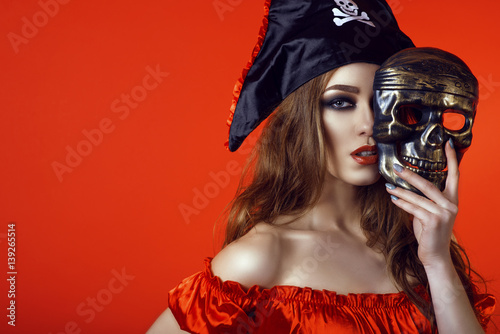 Fotografia, Obraz Portrait of gorgeous sexy woman with provocative make-up in pirate costume hiding the half of her face behind skull mask
