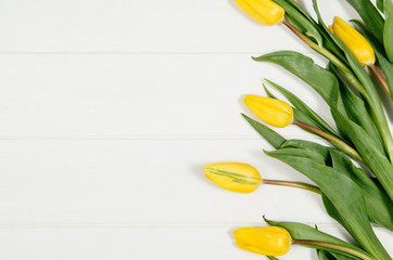 Poster - Background with yellow tulips on white wooden table top view. Creative woman's workspace concept with copy space. Product photograph taken from above with frame composition