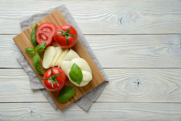 Wall Mural - Mozzarella and tomato with basil leaves on a white wooden background